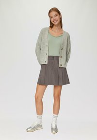 Hellgrauer Cardigan mit strukturiertem Strick, grünes Oberteil mit gewellten Kanten, grauer Nadelstreifenrock und silberne Turnschuhe mit weißen Socken.