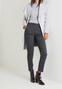 Grå ullkappa med öppen framsida, grå stickad tröja, rutiga grå byxor och glansiga burgunderfärgade ankelskandaler med blockklack.