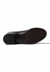 Suela de zapato de cuero negro con una superficie texturizada, bordes lisos y un tacón plano. Incluye un detalle de logo en relieve cerca de la zona del tacón.