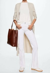 Cardigan beige, t-shirt blanc, jeans blancs évasés et sac en cuir marron. Les baskets sont de couleurs claires avec une semelle texturée.