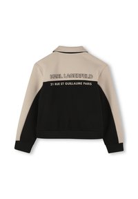 Veste zippée noire et beige avec un col. Présente "KARL LAGERFELD" et "21 RUE ST GUILLAUME PARIS" imprimés à l'arrière. Tissu doux.
