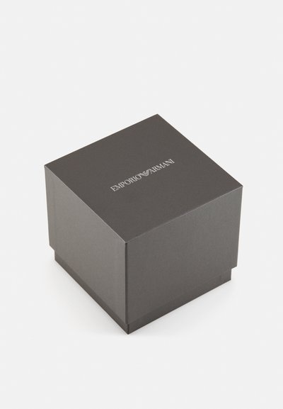 Boîte en carton grise de forme carrée, avec un logo en relief argenté "Emporio Armani" sur la surface supérieure. Texture lisse et mate.
