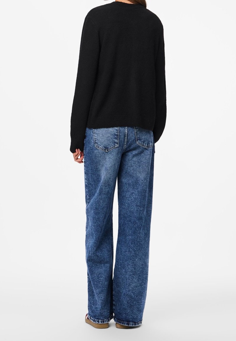 Suéter negro de punto con cuello redondo, combinado con pantalones vaqueros de mezclilla azul claro de corte holgado, con un acabado desgastado y bolsillos traseros.