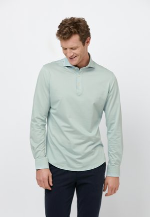 Lange mouwen, licht muntgroene polo met een knoopkraag, gladde stof en een ontspannen pasvorm. Kenmerkt zich door een gebogen zoom en knoopaccenten.