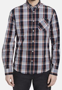 Chemise à manches longues à carreaux dans les tons marine, gris et crème avec des accents orange. Col boutonné et poche poitrine unique avec motif diagonal.