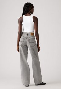 Grijze wijd uitgesneden jeans met een hoge taille, met een bruine leren patch aan de achterkant en klassieke stiksels op de zakken.