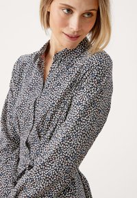 Hemd mit Knopfleiste aus dunkelblauem Stoff, der ein mehrfarbiges abstraktes Muster aufweist, lange Ärmel und einen Kragen hat. Taillierter Schnitt.