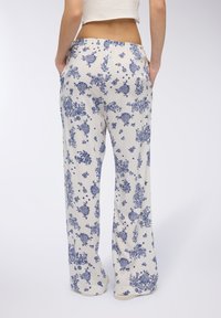 Pantaloni bianchi con motivo floreale e disegni blu, a gamba ampia, con vita elastica e tasche laterali. Tessuto morbido con texture liscia.