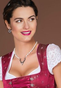 Traditionelles Dirndl aus dunkelrosa Satin mit floralem Muster, weißen Spitzenärmeln, akzentuiert durch eine Perlenkette mit einem Geweihanhänger.