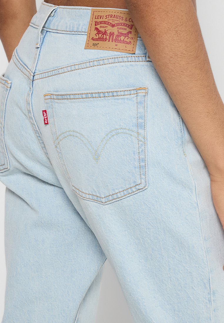 Lichtblauwe spijkerbroek met een hoge taille, achterzakken met kenmerkende stiksels en een tan leren patch met het merklogo op de tailleband.