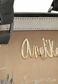 Braune Kunstleder-Handtasche mit einem metallisch goldenen "Amelia"-Logo, besetzt mit Strasssteinen und einem strukturierten silbernen Rand.