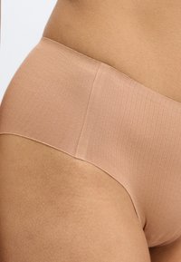 Μπεζ ριμπ υφής εσώρουχο hipster, με λεία υφή και μαλακή ελαστική ζώνη μέσης, σχεδιασμένο για άνεση και διακριτική εφαρμογή.