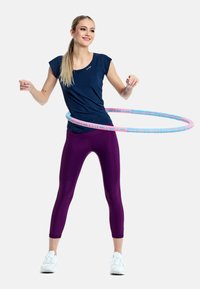 Bluză scurtă de navigație, colanți viola și pantofi sport albi. Cerc de hula cu accente roz și albastre. Persoană într-o poziție activă.