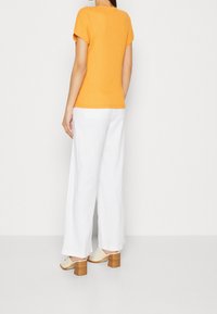 Top naranja de manga corta combinado con pantalones anchos blancos y mules de tacón bloque beige. Textura de algodón; diseño de ajuste relajado.