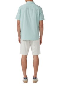 Hellblaues Kurzarm-Hemd mit Knopfleiste aus strukturiertem Stoff, kombiniert mit weißen Shorts und beigen Turnschuhen mit marineblauen Akzenten.