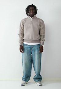 Hellgrauer Quarter-Zip-Sweatshirt, lockere blaue Jeans mit verblasster Textur und weiße Sneakers mit grauen Akzenten. Einfacher Schichtlook.
