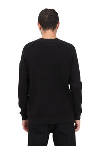 Maglione nero lavorato a maglia con un motivo testurizzato, maniche raglan e polsini a costine. Caratterizzato da una toppa con logo sulla manica sinistra.
