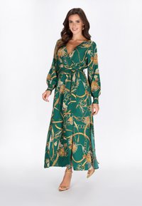 Vestido largo verde envolvente con cadena dorada y patrón floral. Cuenta con mangas largas, cinturón en la cintura y una tela fluida y texturizada.