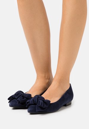 Ballerines en daim bleu marine avec un grand accent de nœud, bout rond et petit talon bloc. Texture lisse avec une silhouette classique.