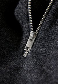 Svart, texturerad tyg med en silverfärgad metalldragkedja, med en mjuk dragtabsdel och synliga tänder tillsammans med en tät, stickad struktur.