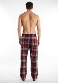 Pantalones de pijama de cuadros rojos y marinos con corte relajado, cintura elástica y tejido suave, vistos desde la parte de atrás. Sin bolsillos.