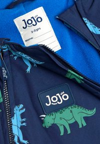 Mørkeblå jakke indvendig med dinosaurtryk i grønt og blåt. Har fleecefór indvendigt og en etikette med størrelse (2-3 år) samt navneskilt.