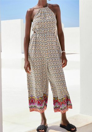 Overal s halter krkem z lehké látky s geometrickými vzory v žluté, modré a bílé; na lemu je barevný květinový vzor.