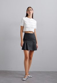 Pull court blanc avec des rayures horizontales texturées, associé à une jupe plissée noire avec des poches. Le mannequin porte des ballerines argentées.
