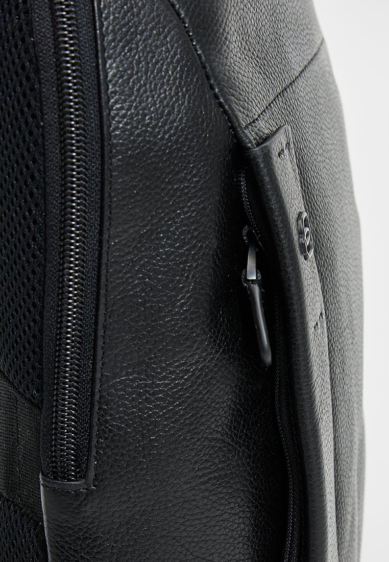 Zwarte leren rugzak met een gestructureerd oppervlak, gaasaccenten en een zijrits. Beschikt over een veilige sluiting en minimalistische designelementen.
