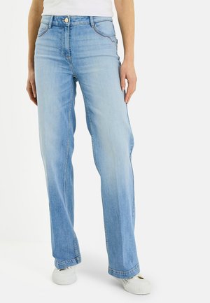 Jean bleu clair à jambes droites porté avec des baskets blanches et un haut blanc rentré, montré de la taille jusqu'aux pieds.