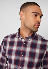 Camisa de cuadros en rojo, azul marino y blanco. Fabricada en un tejido texturizado con cuello y parte delantera abotonada. Presenta un patrón a cuadros.