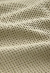Vaffelmönstrad tyg i dämpad beige färg, med ett rutmönster och mjuk, flexibel textur. Idealisk för lätta plagg.