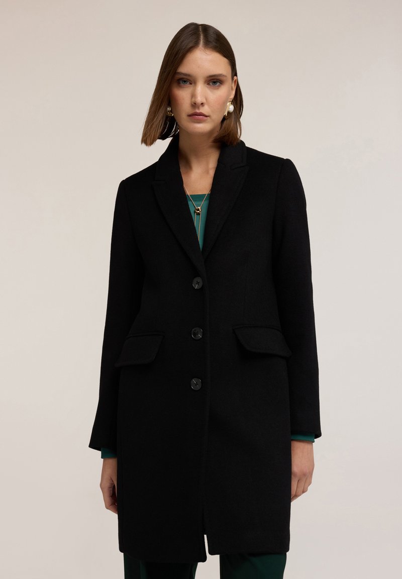 Cappotto in misto lana nera con design sartoriale, rever a punta, tre bottoni e due tasche frontali. Tessuto liscio, vestibilità di lunghezza media.