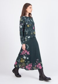 Floral-patterned sweater and skirt set in dark green with pink, white, and yellow accents. Smooth texture and long sleeves. Black ankle boots.