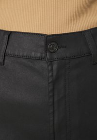 Sorte denimbukser med slim fit, med knappeåpning og toppsøm detaljer. Stoffet har en subtil tekstur og en lett glans.