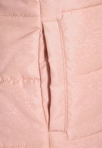 Tissu de veste rose rembourrée avec un motif texturé subtil, dotée d'une poche zippée verticale et de coutures en surpiqûre.