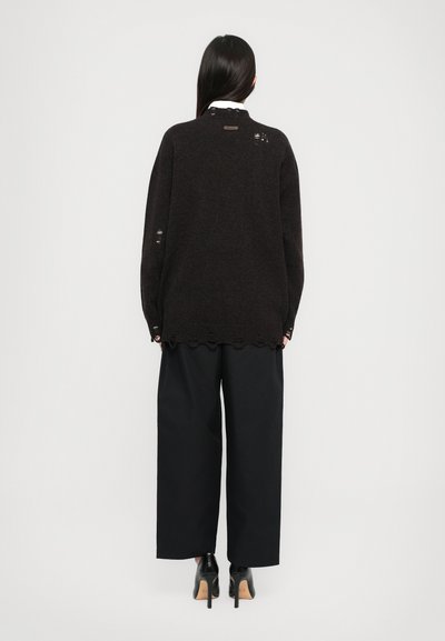 Black knitted sweater with a loose fit, featuring a scalloped hem, visible stitching details, and a round neckline. Paired with wide black pants.