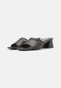 Sandales à glissière ouvertes noires avec une tige en synthétique lisse, présentant un design découpé et un talon bloc géométrique. Semelle intérieure texturée.