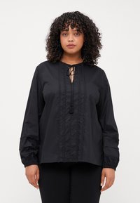 Svart skjorte med knapper og knyting i halsen, frontklaff, teksturert kant og elastiske ermer. Stoffet ser glatt ut med en lett glans.