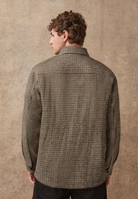 Camicia a scacchi in tonalità marroni e beige, con colletto, maniche lunghe e una texture morbida. La vista posteriore mostra chiaramente il motivo.