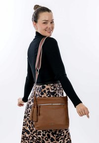 Brown leather crossbody bag with a zippered pocket and tassel detail, featuring a textured finish and adjustable strap.