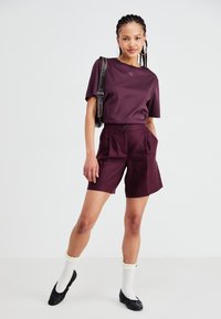 Mauve t-shirt with a small logo, paired with tailored mauve shorts, featuring a front button, side pockets, and finished with black flats.