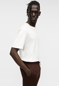 Λευκό κοντομάνικο μπλουζάκι από μαλακό ύφασμα, συνδυασμένο με καφέ παντελόνια με κορδόνι στη μέση και πλαϊνές τσέπες. Απλός σχεδιασμός και άνετη εφαρμογή.