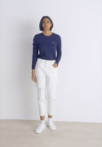 Marine langermet skjorte, hvite slitte jeans og hvite joggesko. Egenskaper inkluderer rund hals og en avslappet passform.
