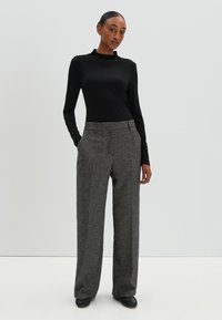 Zwarte langharige top met een hoge hals, gecombineerd met grijze wollen wijde broek met een klassiek patroon en zijzakken.