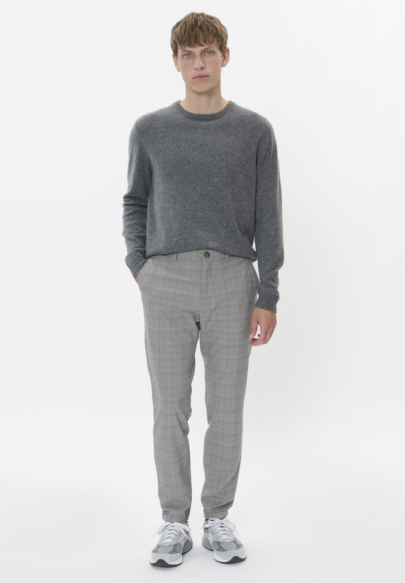 Suéter de punto gris, pantalones ajustados con patrón de cuadros en gris y beige con un botón, y zapatillas gris con acentos blancos.