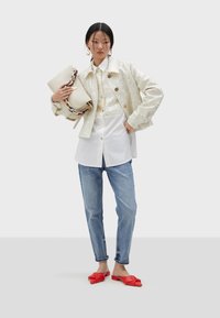 Cream-colored sequin jacket, white shirt with buttons, light blue jeans, and red flat shoes. Holding a beige bag with a braided handle.