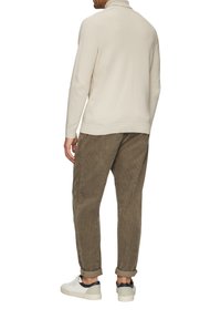Helle beige, strukturierte Strickjacke mit hohem Kragen, kombiniert mit braunen Cordhosen. Weiße Sneakers mit marineblauen Akzenten runden das Outfit ab.