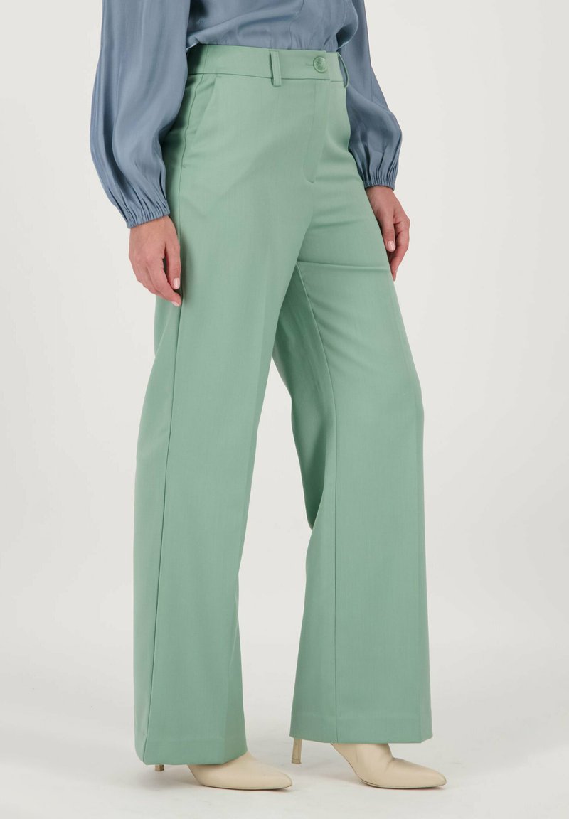 Mintgroene wijde broek gemaakt van soepel materiaal, met een knoopsluiting in de taille en een getailleerde pasvorm, gecombineerd met beige puntige hakken.