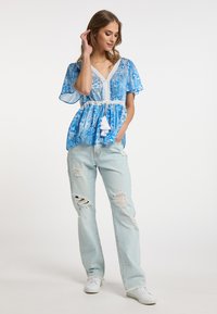 Blusa blu a fantasia con pizzo, maniche a farfalla corte e vita con cordoncino. Indossata con jeans chiari strappati e sneakers bianche.